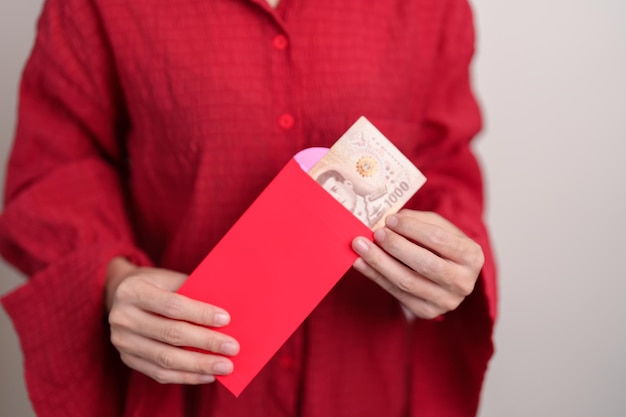 幸せな旧正月の休日のためのタイのバーツのお金の贈り物で中国の赤い封筒を保持している女性