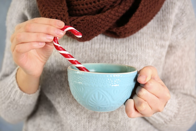 Woman holding Christmas candy cane and cup in hands