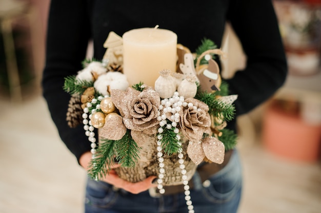 Woman holding a Christmas composition made of candle, beige roses, balls and beads and fir tree