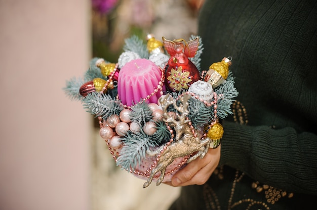 Woman holding a Christmas composition made of fir tree, colorful glass balls and toys