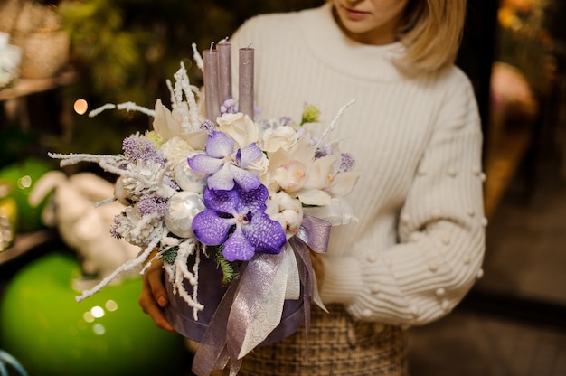 Woman holding a christmas composition with purple and white orchids and roses