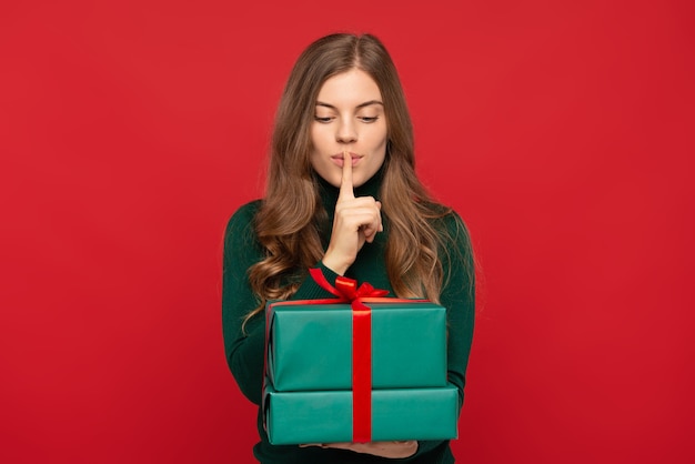 Photo woman holding christmas gift and showing silence sign