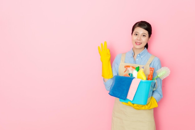 woman holding cleaning stuffs with toothy smile isolated on pink background