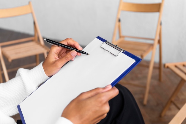 Photo woman holding clipboard at a group therapy session with empty chairs