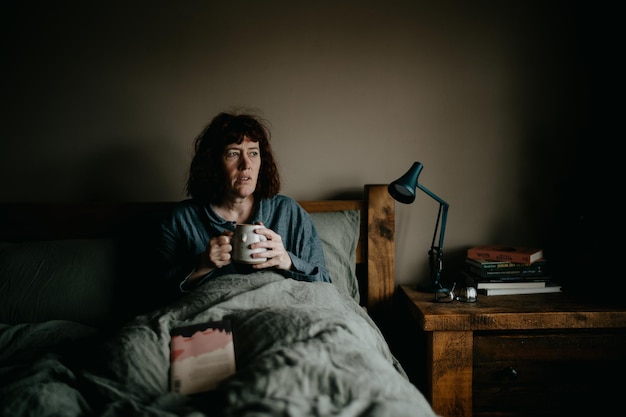 사진 커피 컵 을 들고 있는 여자 가 집 에서 침대 에 누워 있다
