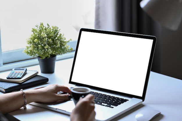 Woman holding coffee cup and working online checking email on computer laptop