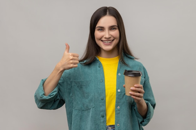 行くためにコーヒーを持って、カメラに親指を見せている女性は、カフェやコーヒーハウスをお勧めします