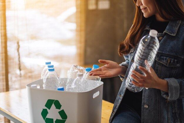 A woman holding and collecting recyclable garbage plastic bottles into a trash bin at home