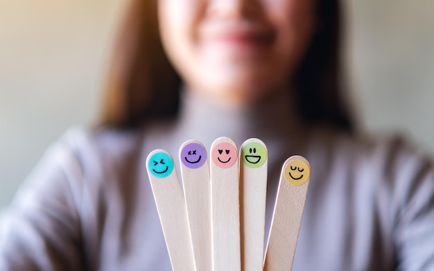 Photo a woman holding colorful hand draw happy emotion faces on wooden stick