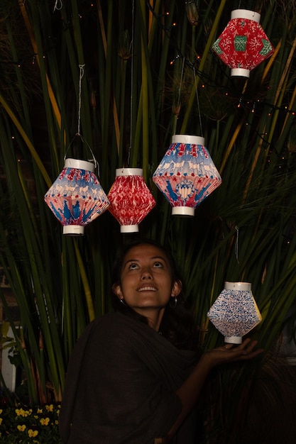 Woman holding a colorful paper lantern while looking at other lanterns hanging on a plant