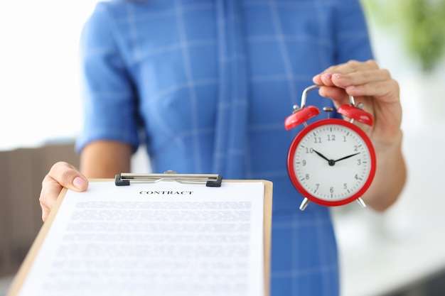 Фото Женщина держит контракт и красный будильник в руках крупным планом график рабочего времени