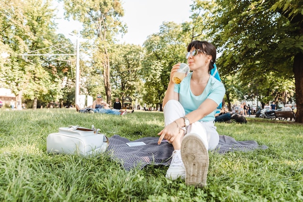 woman holding cool drink in city park blurred background wide angel