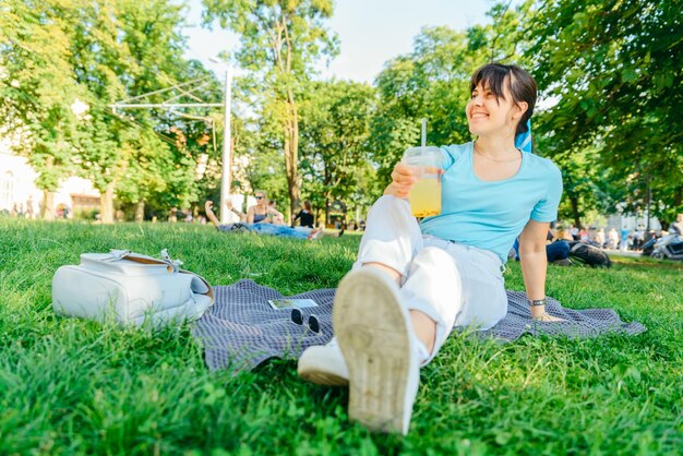 Woman holding cool drink in city park blurred background