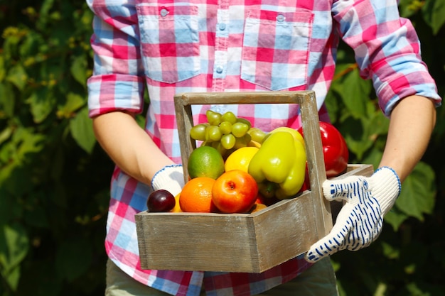 Женщина держит ящик с фруктами и овощами на открытом воздухе