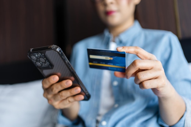 クレジットカードを持って、自宅でスマートフォンを使用している女性