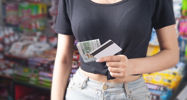 Woman holding credit card and money at supermarket.