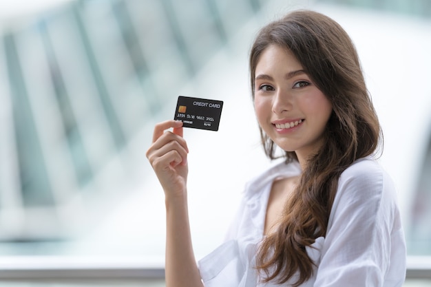 Woman holding credit card and smiling near the store during shopping process