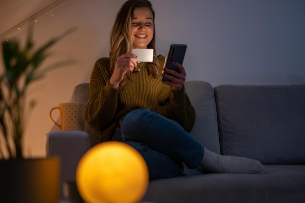 Donna che tiene la carta di credito e utilizza lo smartphone mentre fa acquisti online a casa