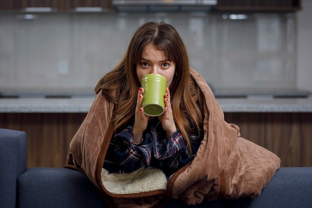 Woman holding a cup of coffee on a cold day covered with a blanket