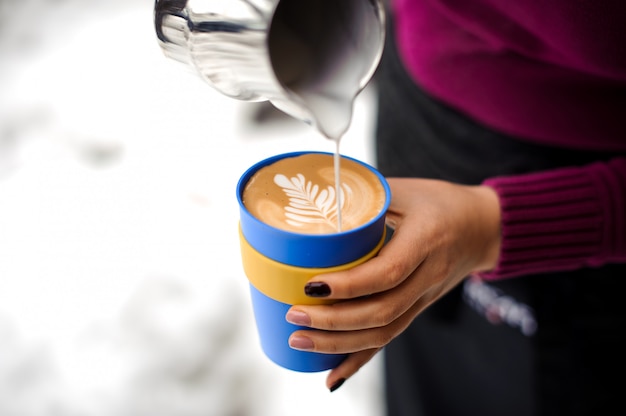 Woman holding a cup of coffee latte and a pitcher in coffee shop