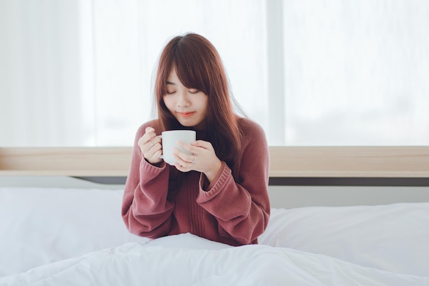 Woman holding a cup coffee tea milk on the bed in a white\
roomwoman drinking