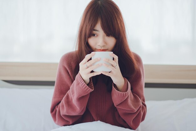 Woman holding a cup coffee tea milk on the bed in a white
roomwoman drinking