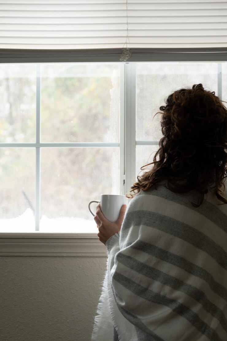 woman holding cup in front of window with snow