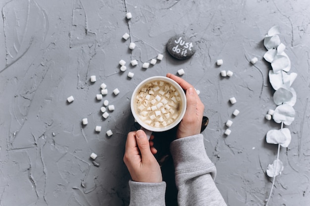 Woman holding cup of hot coffee, closeup photo of hands in warm sweater with mug, winter morning concept, top view