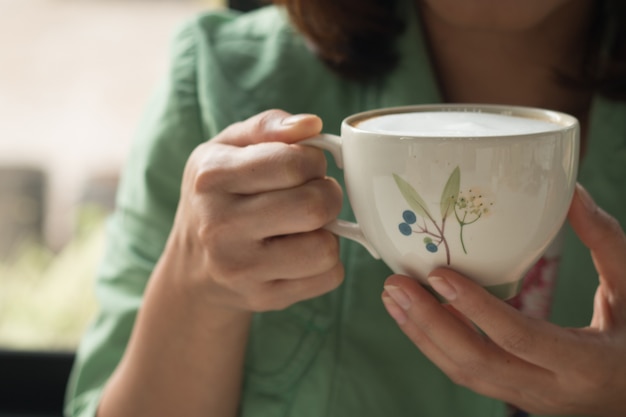 Una donna che tiene una tazza di caffè caldo latte nel caldo giorno del mattino