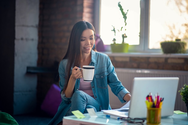 Woman holding a cup with tea while working on the laptop