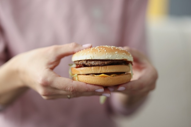 Donna che tiene un delizioso hamburger appetitoso nel suo primo piano delle mani