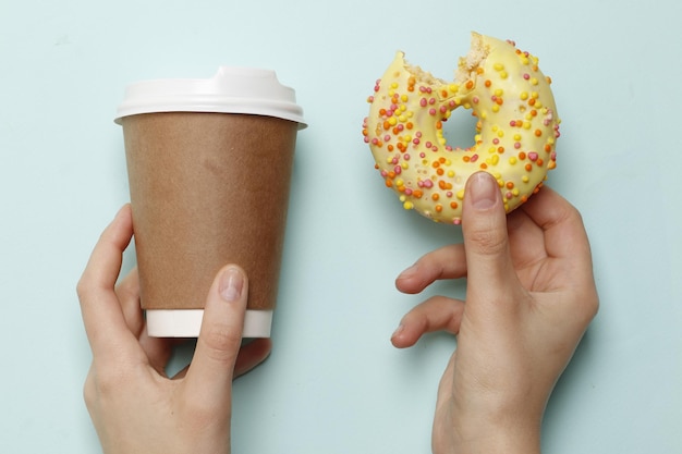 Woman holding delicious donut and coffee on color background