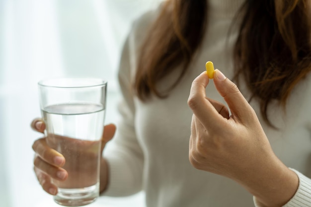 A woman holding a dietary supplement or medication and a glass of water ready to take medicine Vitamin health of people