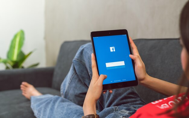 Woman holding digital tablet and pressing the Facebook screen