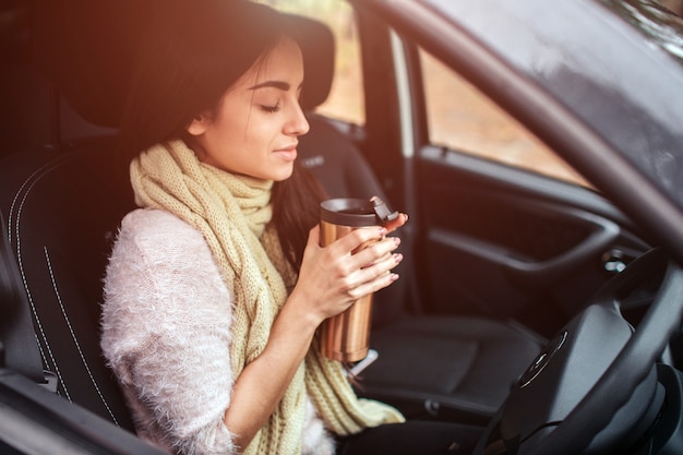 woman holding disposable cup of coffee in car.