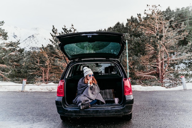 Photo woman holding dog while sitting in car trunk