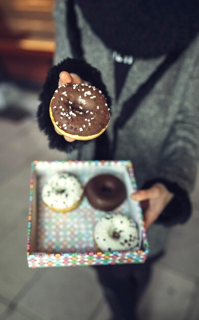 Woman holding doughnut with chocolate icing, partial view