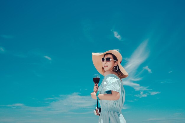 Woman holding drink while standing against blue sky