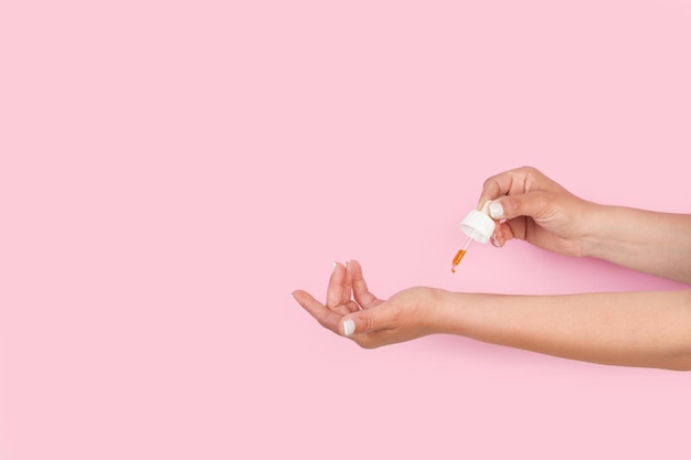 Woman holding a dropper with essential oil on her wrist on a pink background with copy space