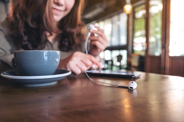 woman holding earphones while listening to music with mobile phone  in cafe