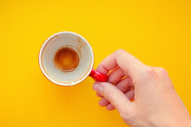 黄色の背景に空のコーヒーカップを保持している女性