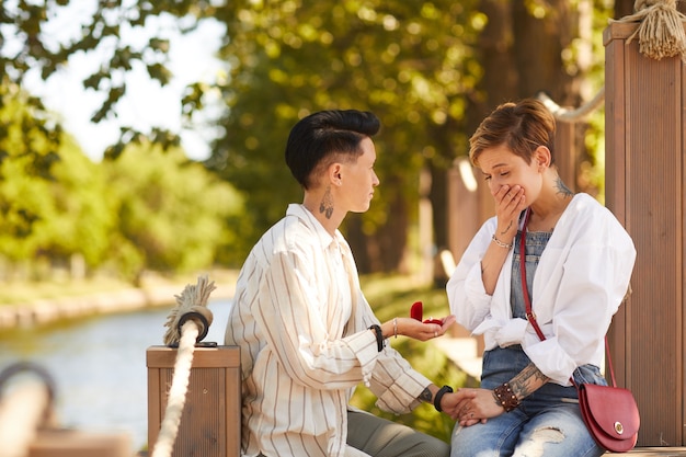 Женщина держит обручальное кольцо и делает предложение своей девушке во время свидания в парке