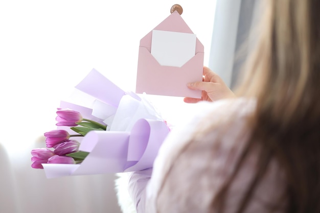 Woman holding envelope with blank greeting card and tulip bouquet at home