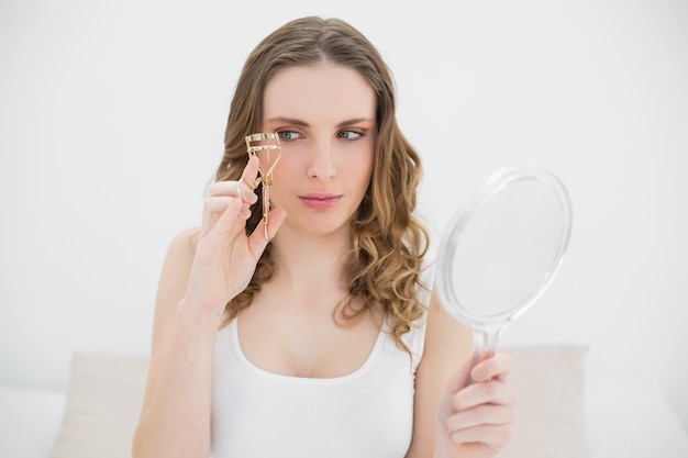 Woman holding an eyelash curler and a mirror