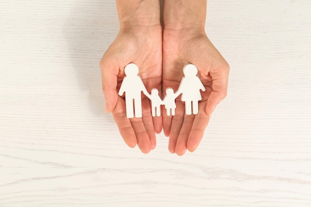 Woman holding figures of family in hands on white wooden background top view