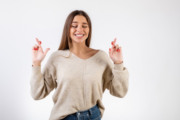 Woman holding fingers crossed praying isolated over white