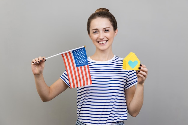 Woman holding flag of united states of america and paper house dreaming about living in usa