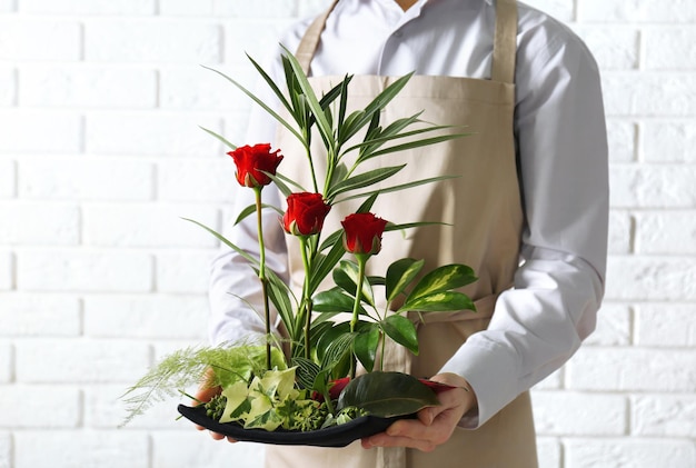 レンガの壁の背景に花の構成を保持している女性