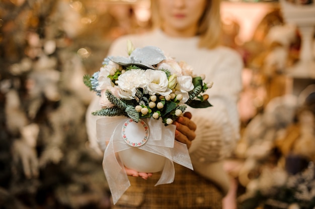 woman holding a flower pot with white flowers decorated wuth green leafs and fir-tree branches