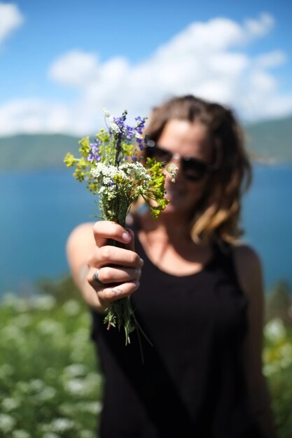 Foto donna che tiene dei fiori contro il cielo